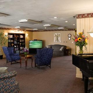 A cozy lounge area with comfortable seating, a television, bookshelves, and a piano.