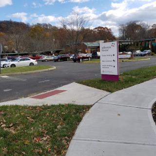 A view of a parking lot with signage and a sidewalk under a cloudy sky.