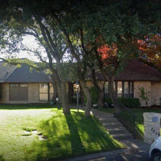 A suburban house with a well-maintained yard and trees casting shadows in the sunlight.