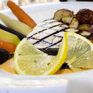 A gourmet plate featuring grilled fish with lemon slices and a side of assorted vegetables.