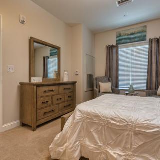A cozy bedroom featuring a neatly made bed, a wooden dresser with a mirror, and a window adorned with curtains.