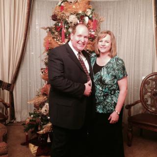 A cheerful couple posing together in front of a beautifully decorated holiday tree.