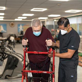 A healthcare professional assists an elderly patient using a walker during physical therapy.
