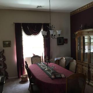 A traditional dining room with a large table, surrounded by chairs and adorned with elegant curtains and a chandelier.
