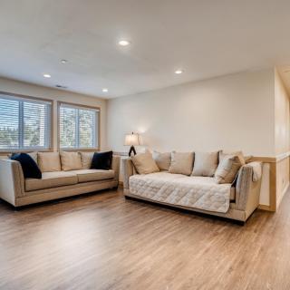 A modern living room featuring two beige sofas, wood flooring, and large windows allowing natural light.
