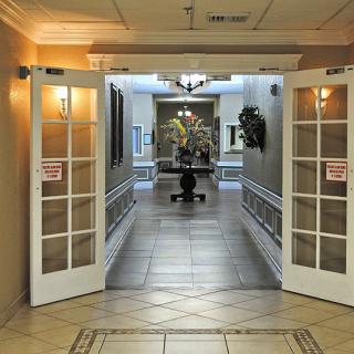 An inviting hallway with open double doors leading to a lobby area, featuring warm lighting and decorative elements.