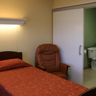 A simple bedroom with a bed, armchair, and an adjoining bathroom.