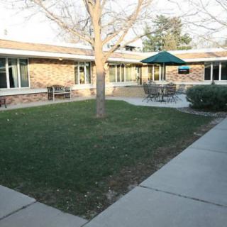 A peaceful courtyard with outdoor seating and a sun umbrella, surrounded by a building.