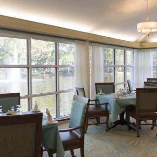 A bright dining room with tables and chairs, featuring large windows that allow natural light to stream in.