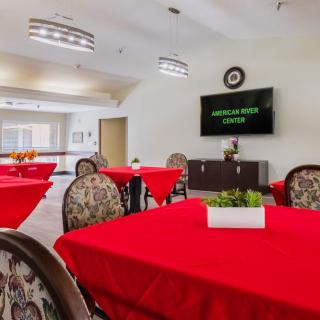 A dining area with red tablecloths, patterned chairs, and a television on the wall.