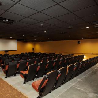An empty auditorium with rows of seats facing a projector screen.