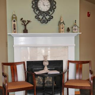 A cozy living room setting featuring a fireplace, elegant wooden chairs, and stylish wall decor.