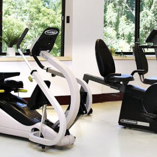 A modern gym space featuring an elliptical machine and a recumbent bike, bathed in natural light from large windows.