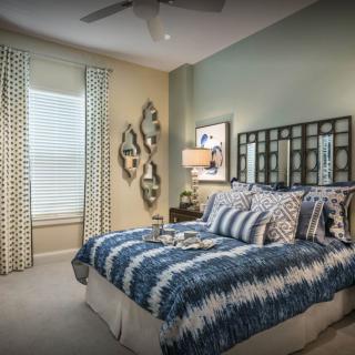 A cozy bedroom featuring blue and white bedding, decorative pillows, a stylish table lamp, and wall art accents.
