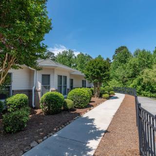 A quaint residential property with a well-maintained sidewalk and lush landscaping on a sunny day.