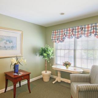 A cozy living room with a table, chair, and large window featuring patterned curtains.