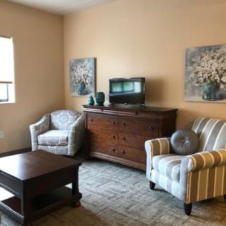 A cozy living room with armchairs, a coffee table, a cabinet with a television, and decorative paintings.