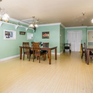 A spacious dining room with wooden furniture and green walls, featuring ceiling fans and a light wooden floor.
