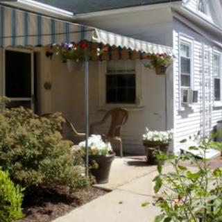 A cozy patio area with a striped awning, surrounded by plants and flowers.