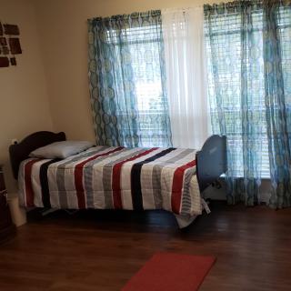A cozy bedroom with a single bed featuring striped bedding, a desk by the window, and soft blue curtains.