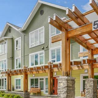 A modern residential building with a wooden pergola and large windows.