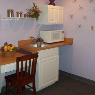 A small kitchen area with a microwave, sink, and wooden chair.