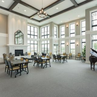 A spacious and elegant dining area with high ceilings, large windows, a chandelier, and a grand piano.