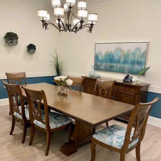 A neatly arranged dining room with a wooden table, six chairs, a decorative chandelier, wall art, and plants.