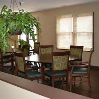 A cozy dining room featuring a large wooden table, comfortable patterned chairs, and a hanging plant near the window.
