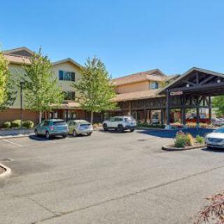 A large hotel building with a parking lot in front, surrounded by trees on a sunny day.