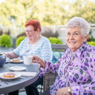 Two elderly women enjoying tea and conversation outdoors.