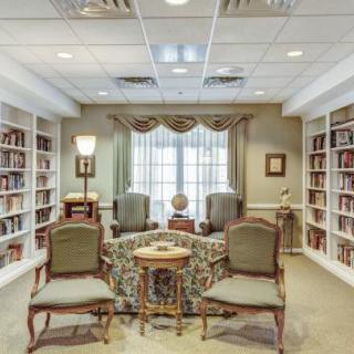 A cozy library reading room with bookshelves, elegant chairs, and a central table.