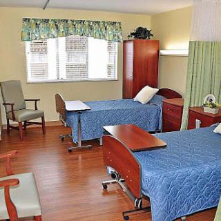 A hospital room with two patient beds, featuring wooden floors and a window with curtains.