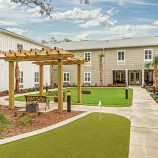 A beautifully landscaped courtyard with a wooden pergola and green lawn surrounded by a modern building.