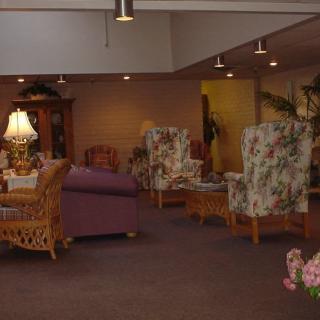 A cozy living room with various seating options, including sofas and floral-patterned chairs, illuminated by lamps.