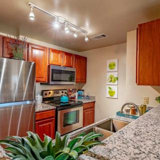 A modern kitchen with stainless steel appliances, wood cabinets, and a granite countertop, featuring track lighting and stylish decor.