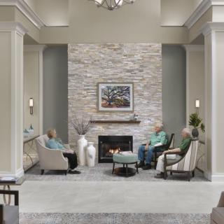 A cozy living room with a modern stone fireplace, where elderly people are seated in comfortable chairs.