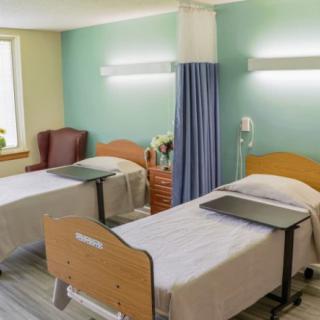 A hospital room with two patient beds equipped with medical trays and a privacy curtain.
