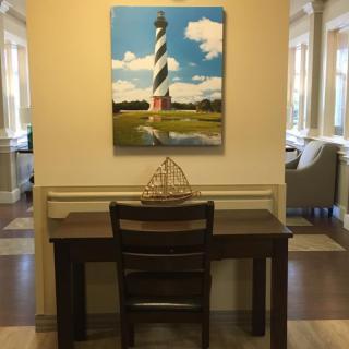 A cozy interior with a desk and chair, featuring a painting of a lighthouse and a model ship decoration.