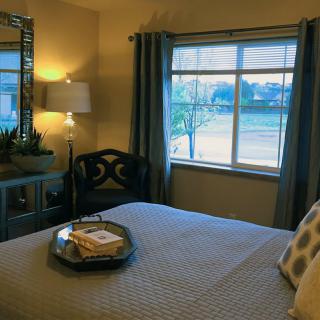 A cozy bedroom featuring a neatly made bed with cushions, a tray on top, and ambient lighting from a lamp by the window.