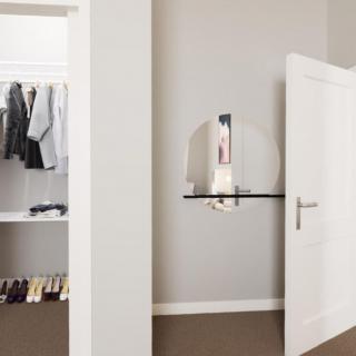 A minimalist room featuring an open closet with neatly hung clothes and a circular mirror on the wall.
