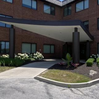 The image showcases the entrance of a brick building with a canopy, surrounded by well-maintained landscaping.