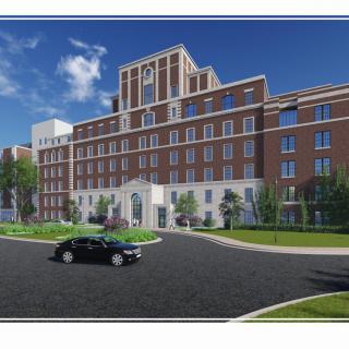 A modern brick hotel building with a central driveway and surrounding greenery on a clear day.