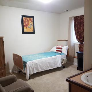 A simple bedroom with a hospital bed, an armchair, and a painting on the wall.