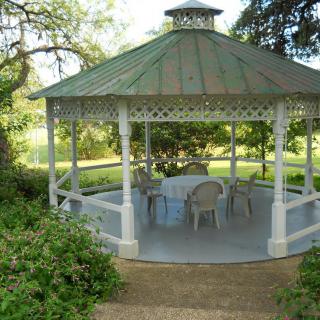 A charming outdoor gazebo surrounded by greenery, furnished with chairs and a table.