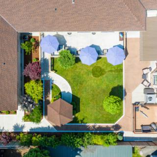 Aerial view of a well-landscaped backyard featuring a green lawn, patio with umbrellas, and garden areas.