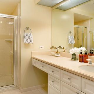 A clean and well-lit bathroom featuring a large mirror, countertop with sink, and a glass-enclosed shower.