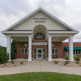 The entrance of Colonial Manor features a classic colonial architectural style with large columns and a welcoming pathway.