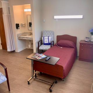 A view of a hospital patient room featuring a bed, chair, and attached bathroom.