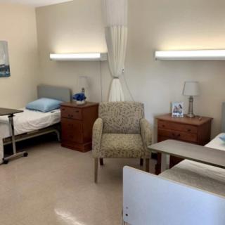 A hospital room with two beds, a chair, and bedside tables.